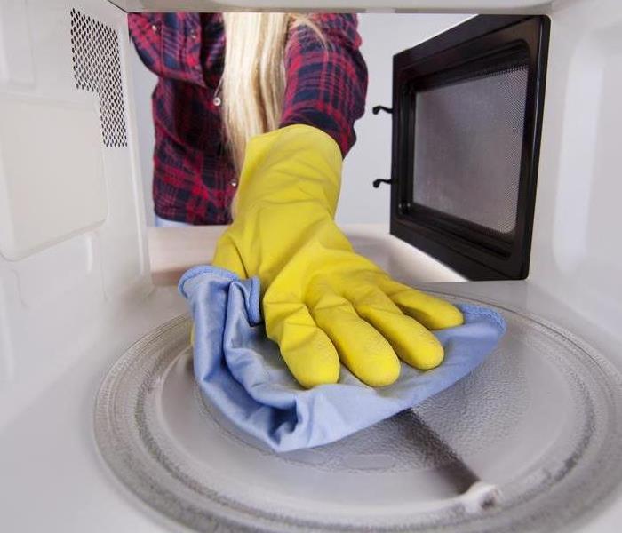 Hand wearing a protective glove wiping a microwave