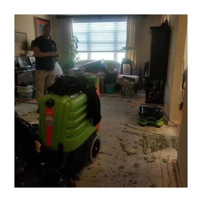 A Servpro technician standing in a living room that has experienced water damage, drying equipment has been placed 