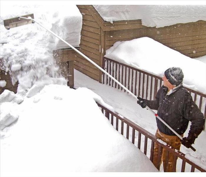 Man removing snow from roof with a rake